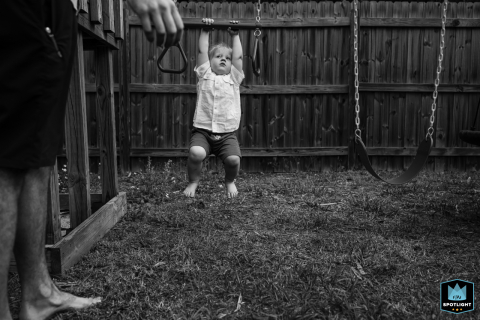 Sarasota, Florida - A black and white shot captures a playful moment of a toddler hanging from a gym bar in his backyard, as captured by a family photographer.